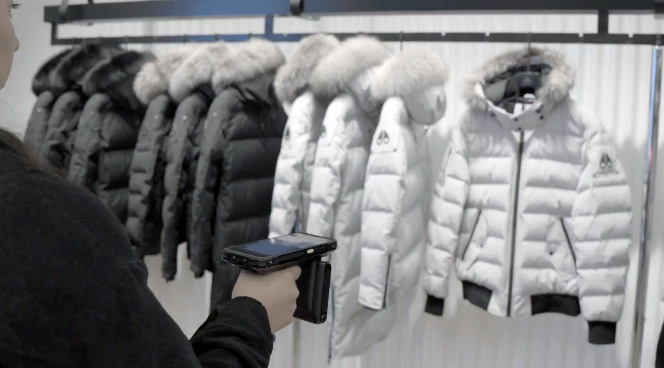 A store associate RFID-scanning a rack of jackets with a handheld reader